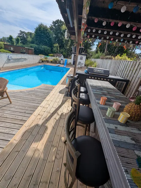 New timber decking beneath an outdoor bar with stools and outdoor kitchen beside a swimming pool in Ayr