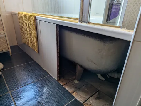 The bathroom before the new panel, with the original tiled bath panel broken out and the side of the bath exposed