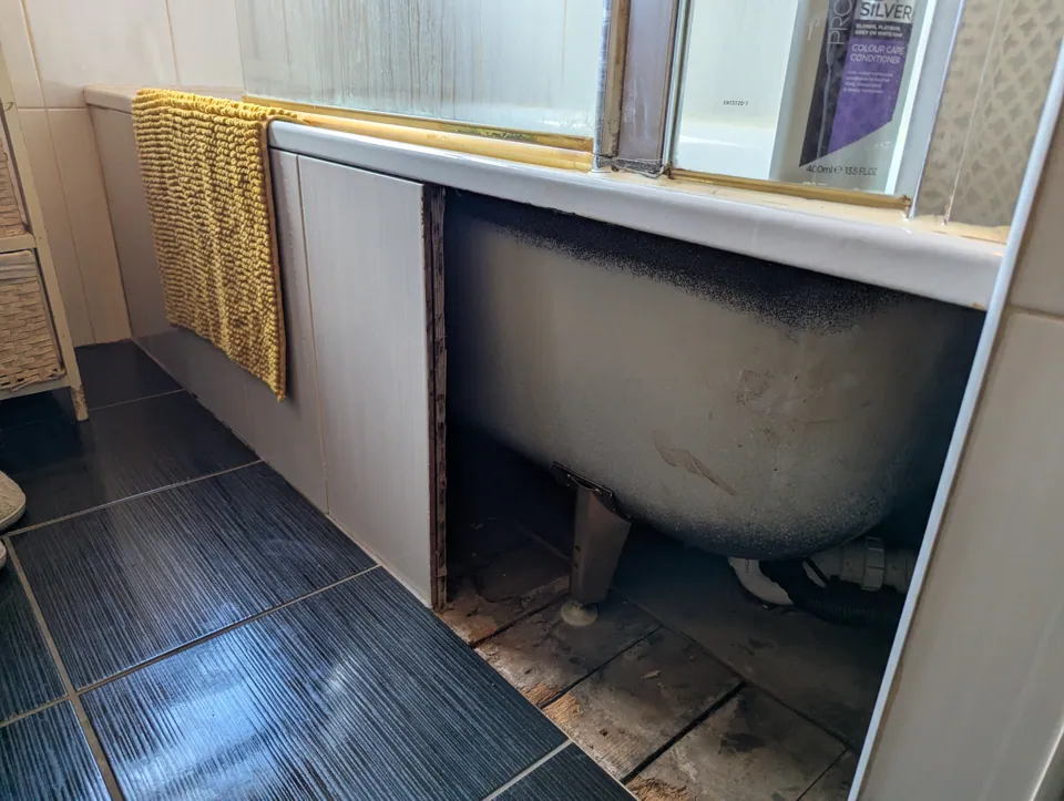 The bathroom before the new panel, with the original tiled bath panel broken out and the side of the bath exposed
