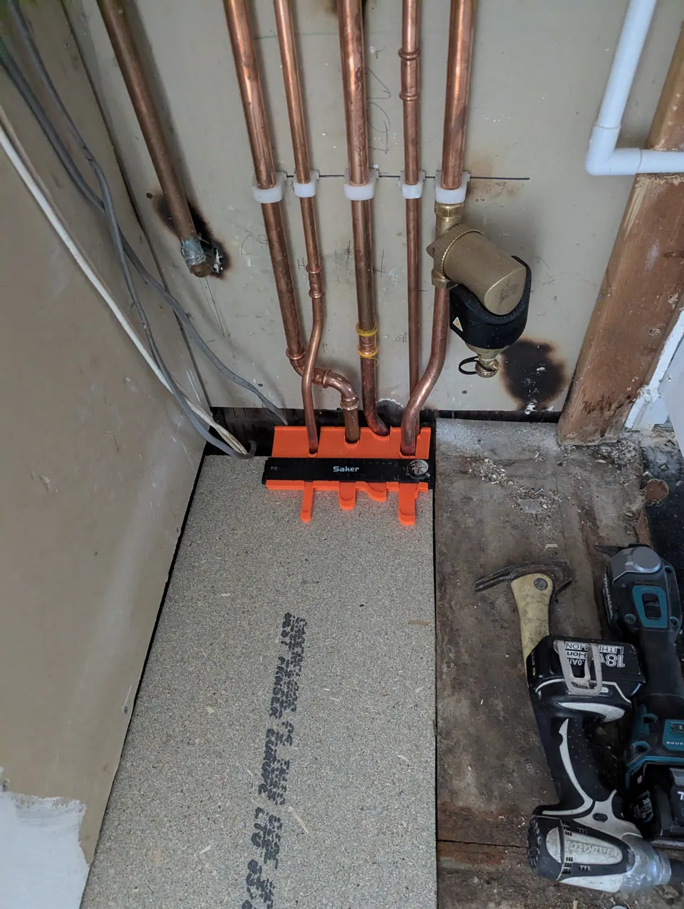 Profile gauge held against five copper boiler pipes to copy their exact shape before cutting the floor decking to suit, in Dreghorn