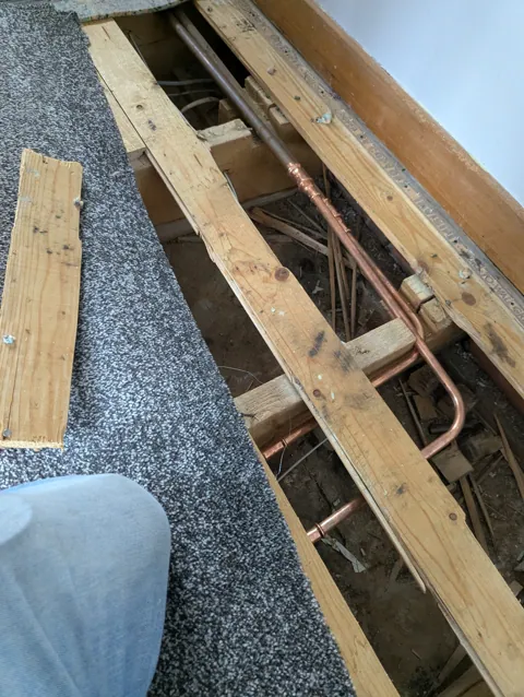 Floorboards lifted at a home in Irvine to give access to copper pipework under the floor after a burst pipe