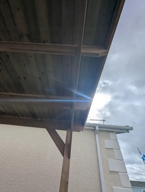 The canopy roof edge and braced post seen against the sky, tied in beside the house