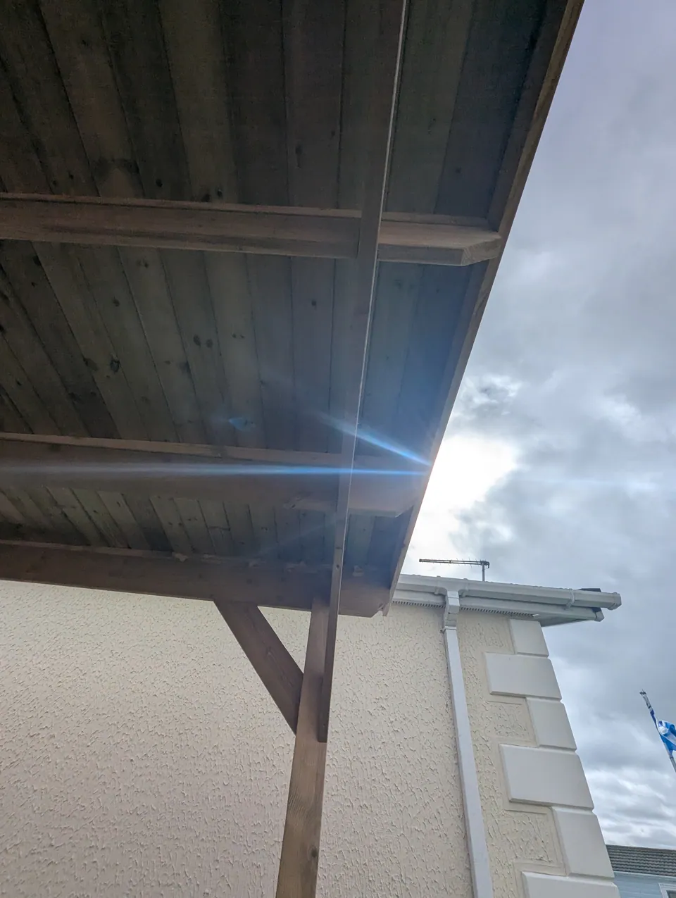 The canopy roof edge and braced post seen against the sky, tied in beside the house