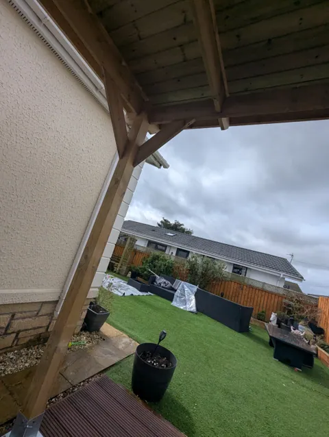 Timber garden canopy built over a patio in Irvine, showing the braced post, beam and boarded roof from beneath