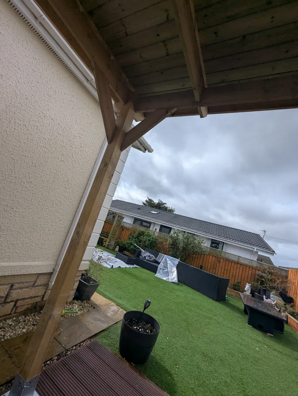 Timber garden canopy built over a patio in Irvine, showing the braced post, beam and boarded roof from beneath