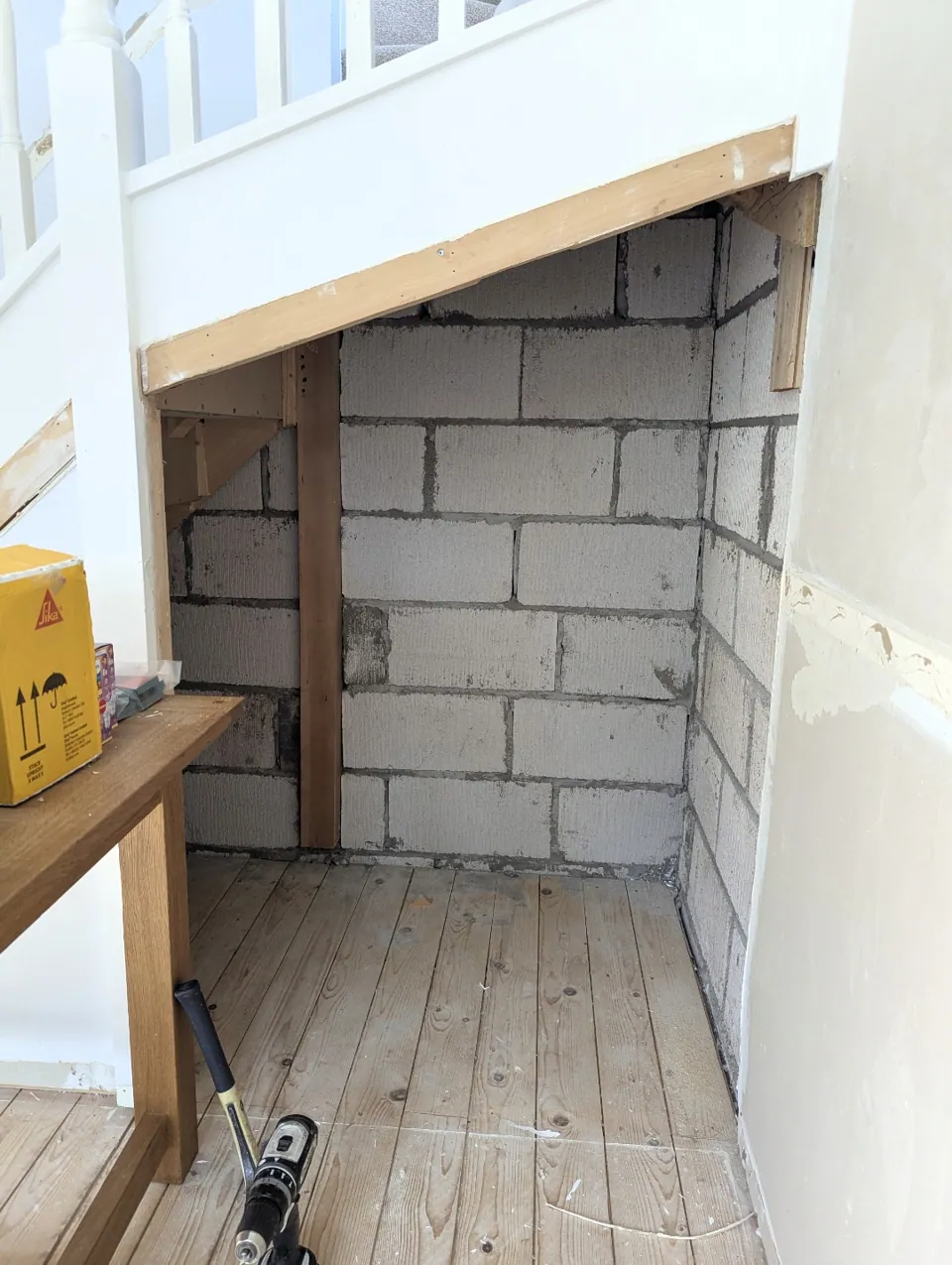 The understairs void opened up before work, with the blockwork exposed and a timber beam across the opening