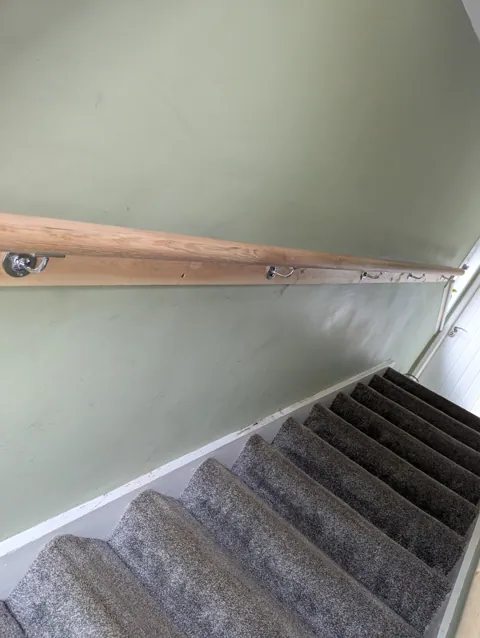Oak mopstick handrail on chrome brackets running up the stair wall, seen from the landing