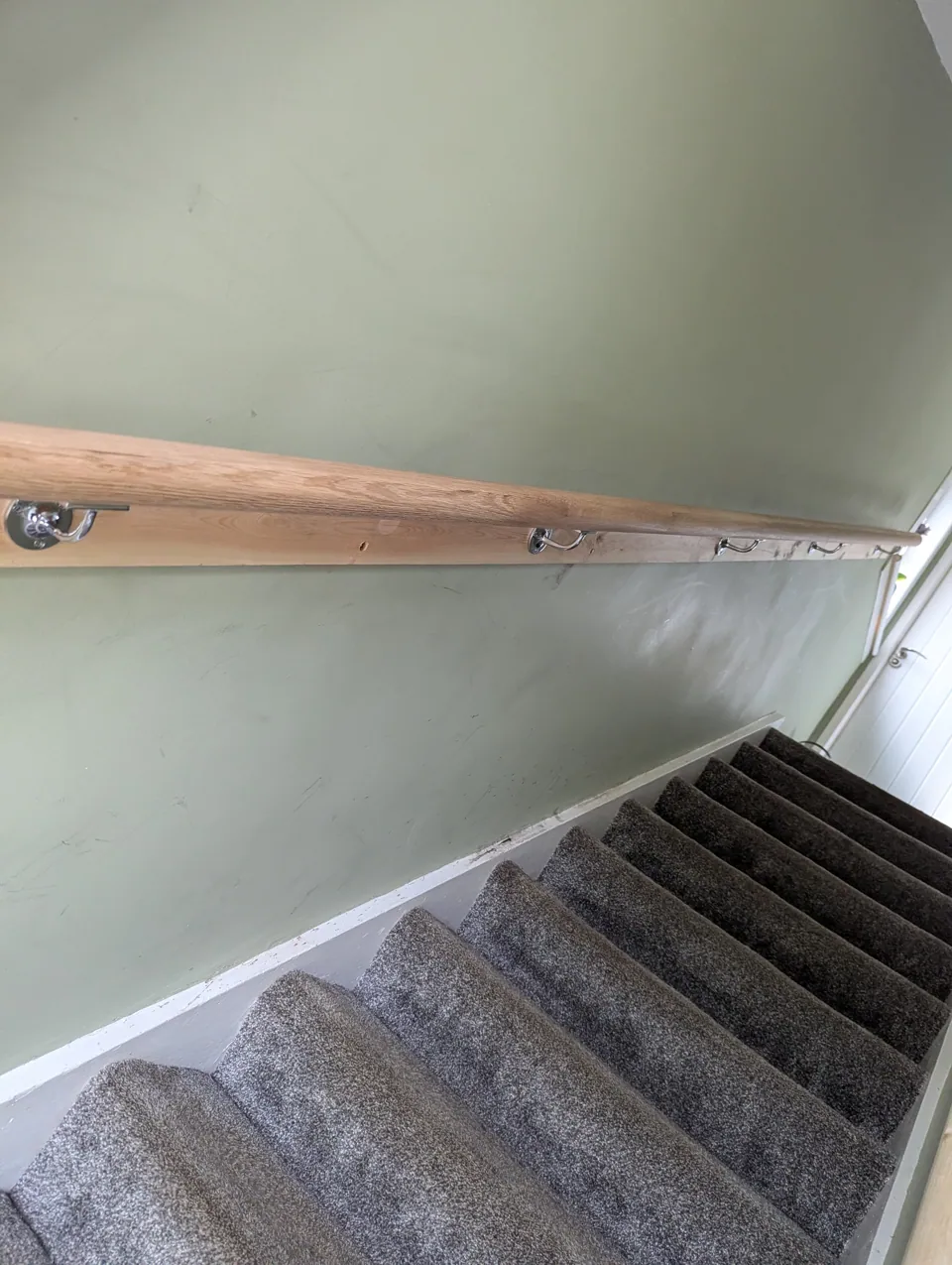 Oak mopstick handrail on chrome brackets running up the stair wall, seen from the landing
