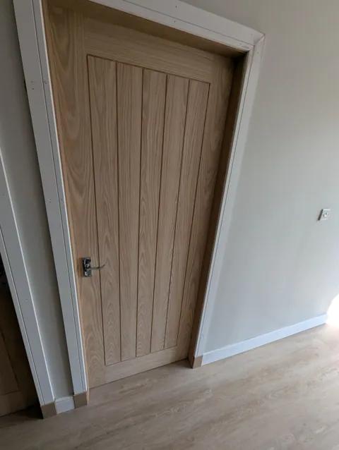 Oak veneered door with chrome scroll lever handle on backplate and new white skirting in Irvine