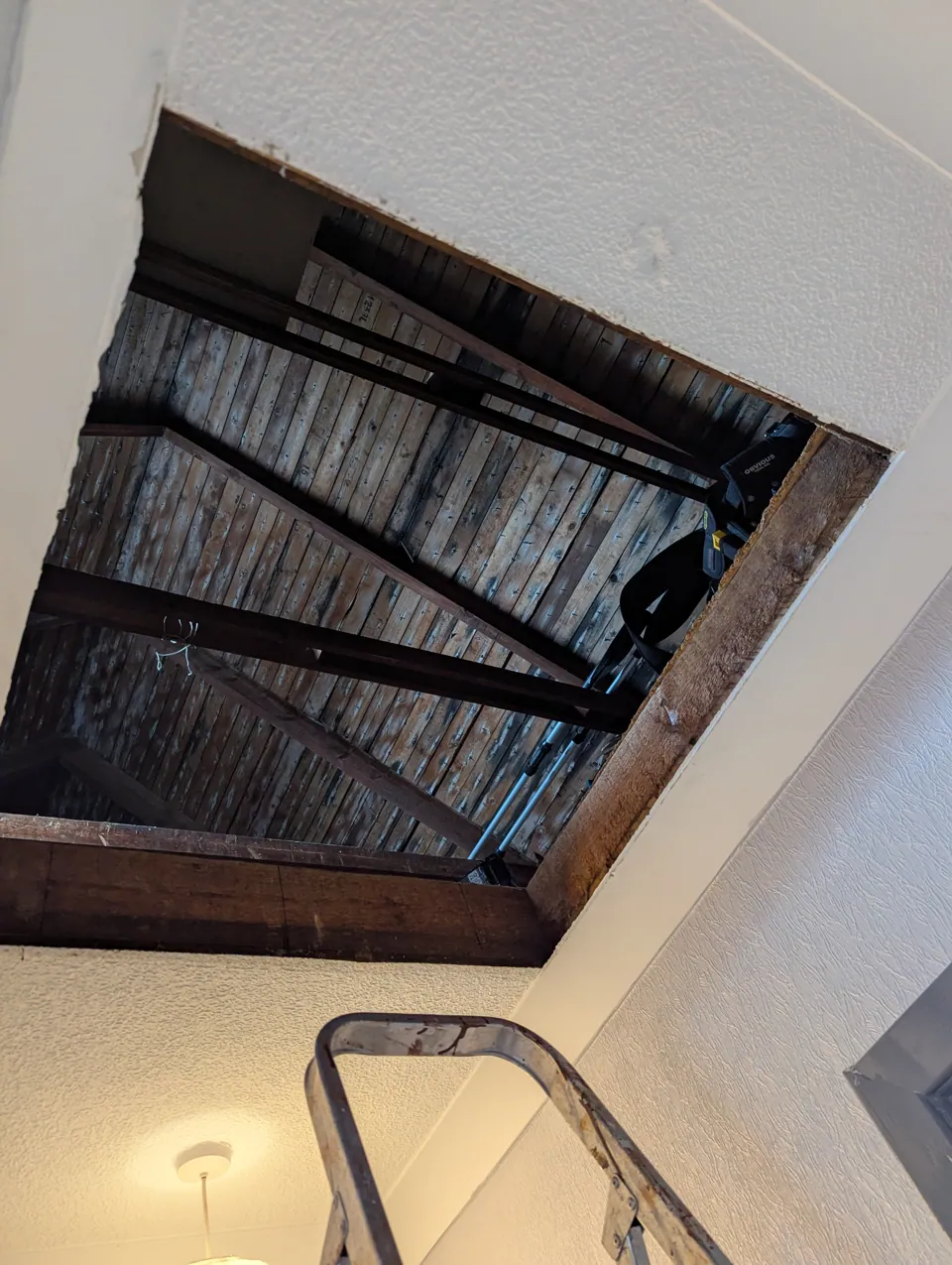 The loft opening being altered, with the roof timbers and joists visible above the ceiling