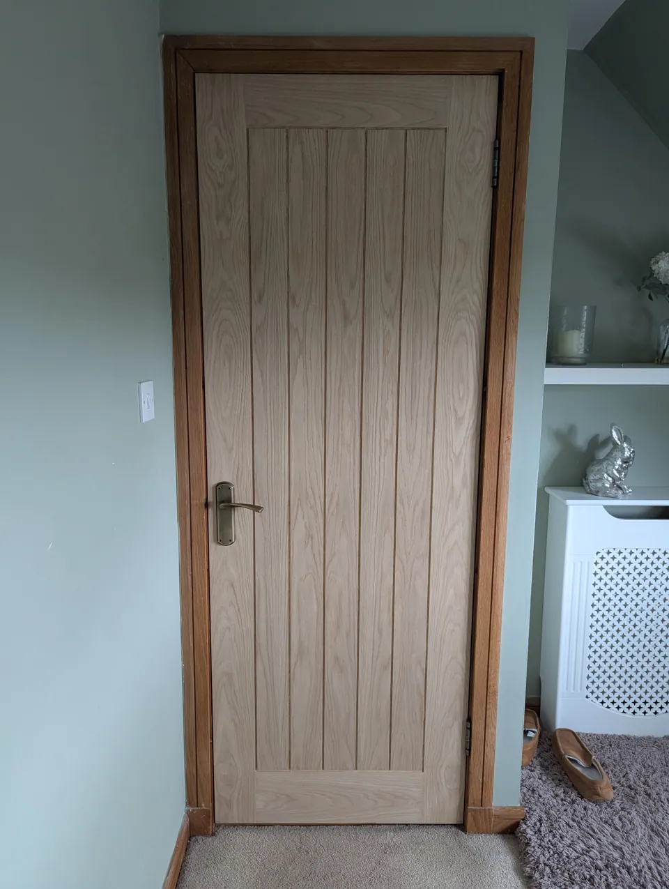 Oak veneered door fitted in a sage green bedroom in Lugton, antique brass handle and matching oak frame