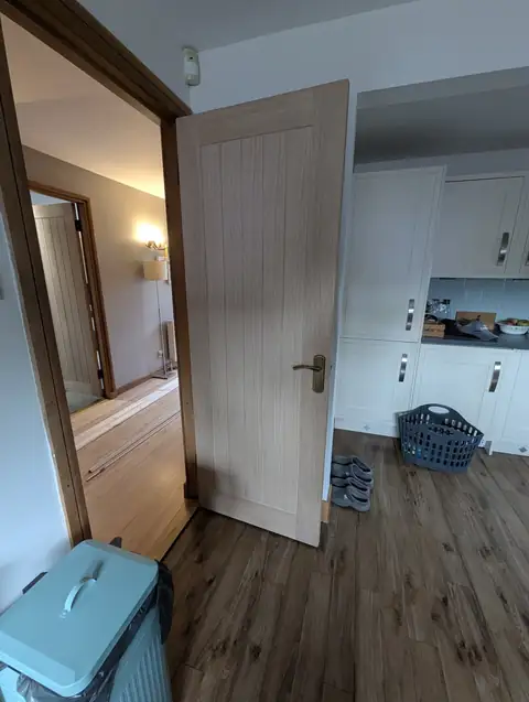 Oak veneer cottage door open through to a kitchen, seen from the hallway