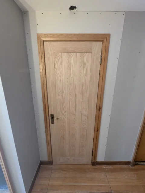 Unfinished oak cottage style door in a solid oak frame set into a new plasterboarded stud wall in Lugton, with antique brass handle