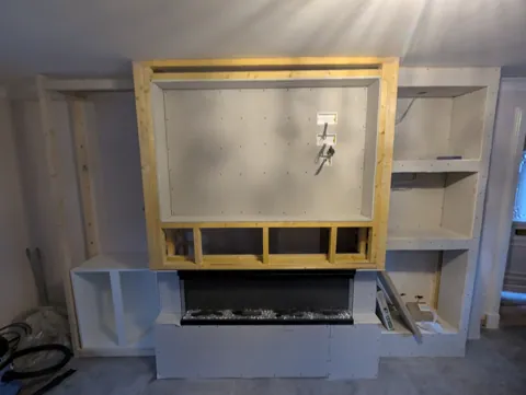 The media wall under construction — timber frame with the TV recess formed and the electric fire set in, before boarding