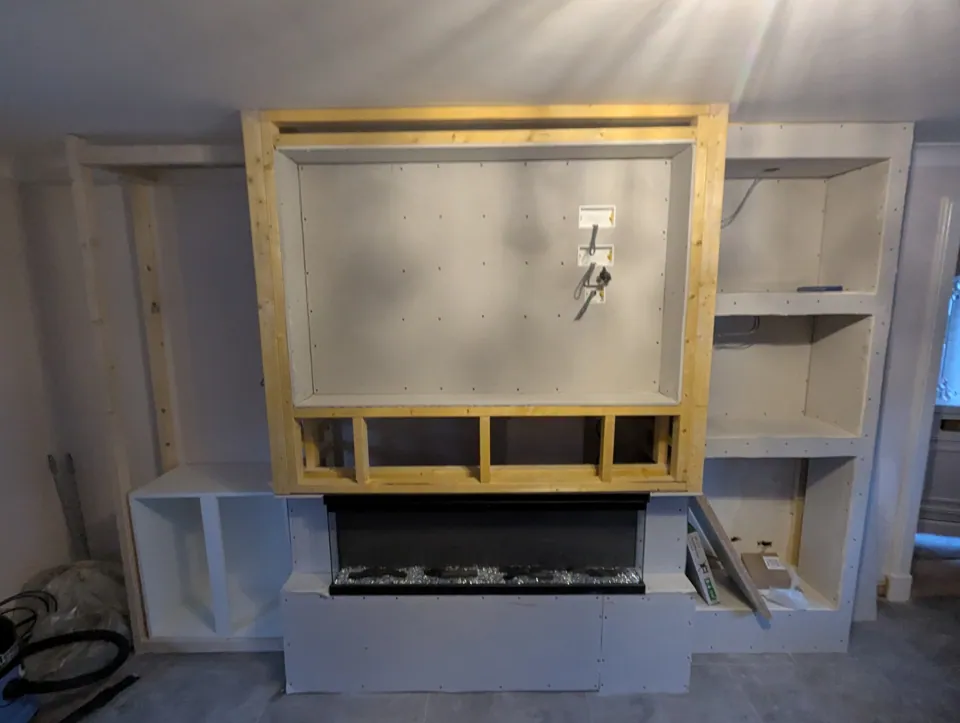 The media wall under construction — timber frame with the TV recess formed and the electric fire set in, before boarding
