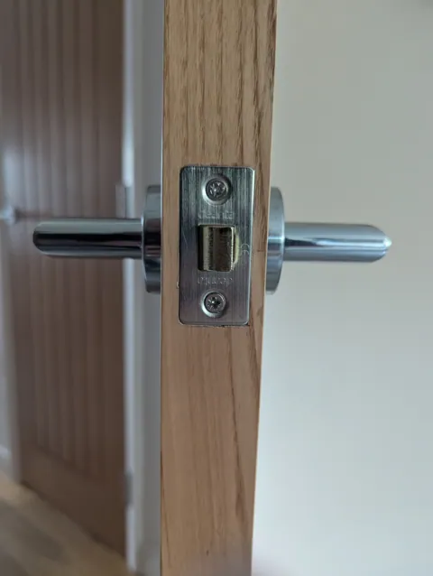 Close-up of a Deanta latch and polished chrome lever handles on a prefinished oak door edge