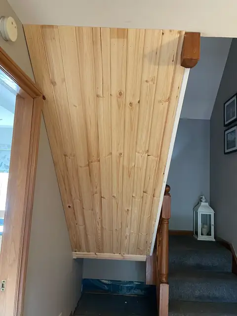 Underside of a staircase lined in V-grooved boarding from top to bottom, seen from the hallway
