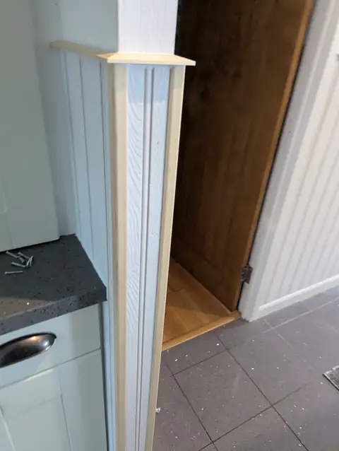 Close view of a timber corner trim and mitred capping rail finishing tongue and groove panelling at a kitchen entrance