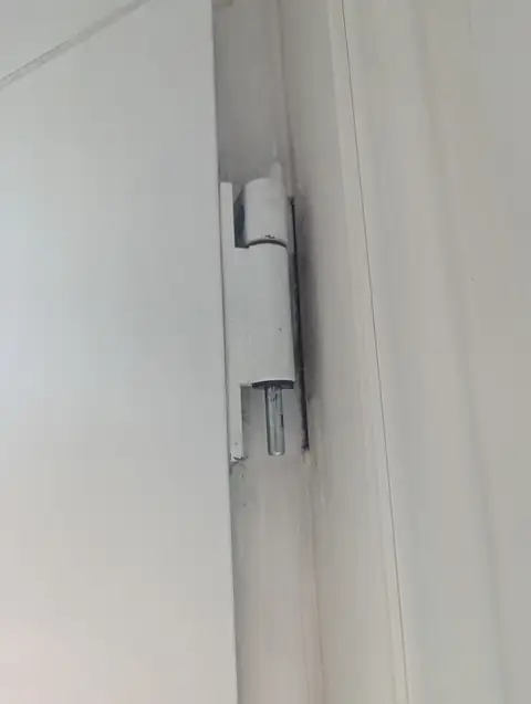 Collapsed top hinge on a white uPVC door, with the hinge pin exposed and the door dropped